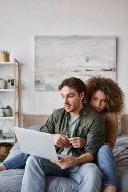 Lovely young couple spending time together in bed with laptop and watching movies clipart