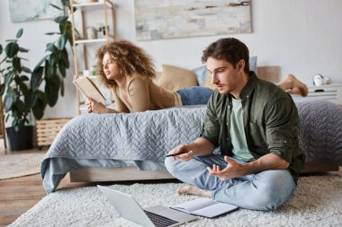 Uzaktan çalışan bir çift. Kadın yatakta kitap okuyor ve erkek internette sohbet ediyor yerde oturuyor.