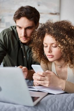 Evden çalışan bir çift. Endişeli adam dizüstü bilgisayara bakıyor kız arkadaşıyla yatakta çalışıyor.