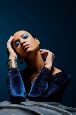 Mavi makyajlı genç Afro-Amerikalı kadın gök mavisi stüdyoda poz veriyor..