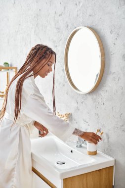 Afro örgülü Afrikalı bir kadın ellerini modern bir banyoda yıkıyor, kişisel hijyen ve kişisel bakım uyguluyor..