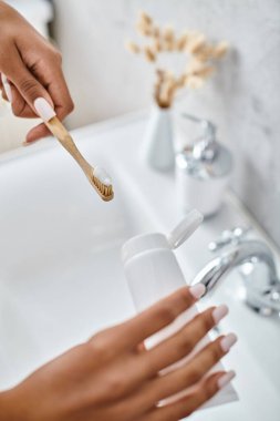 An African American woman in a bathrobe brushes her teeth in a modern bathroom. clipart