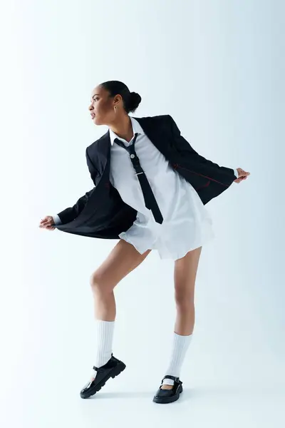 stock image Young African American woman dressed in a white dress and black jacket, strikes a pose