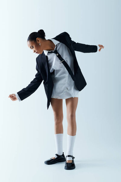 Молодая афроамериканка занимает уверенную позу в стильной рубашке и пиджаке в студии.