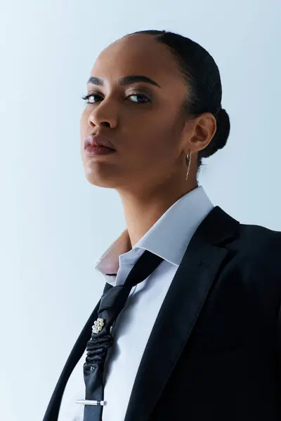 stock image Young African American woman wearing a suit and tie, gazes off to the side in a studio setting.