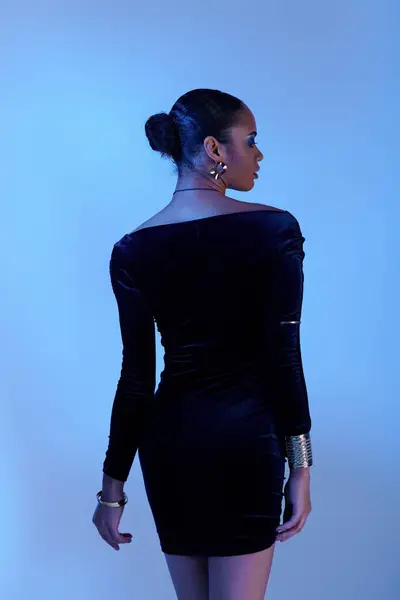 stock image A young African American woman stands gracefully in a black dress in a studio setting