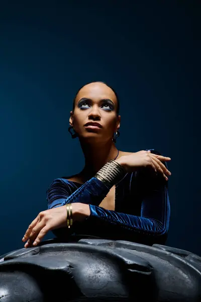 stock image A young African American woman gracefully seated on top of a sleek black object in a studio setting.