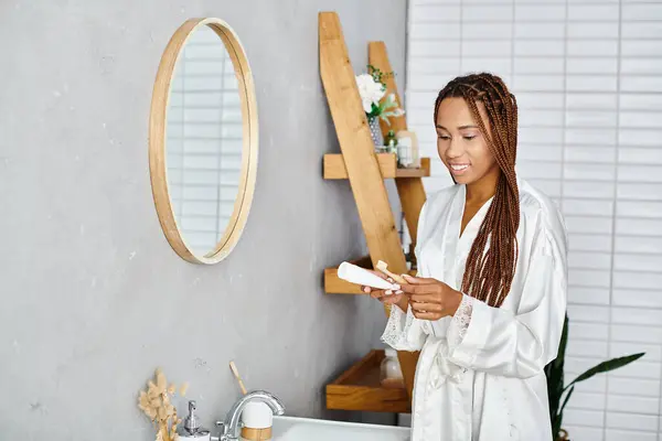 一位戴着非洲式辫子的非洲裔美国女人站在她的现代浴室里 专注于洗澡间里的美感和卫生习惯 — 图库照片