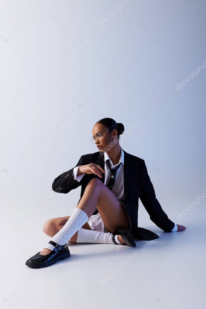 Young African American woman sitting on ground in suit and tie, white studio