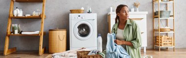 Afro örgülü Afrikalı bir kadın banyoda çamaşır yıkama makinesi ve kurutma makinesiyle çamaşır yıkıyor..