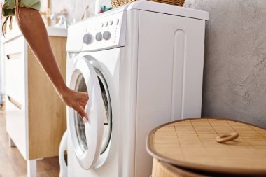 Afro-Amerikalı bir kadın çamaşır makinesini fayansları ve beyaz duvarları olan temiz bir çamaşır odasına yerleştiriyor..