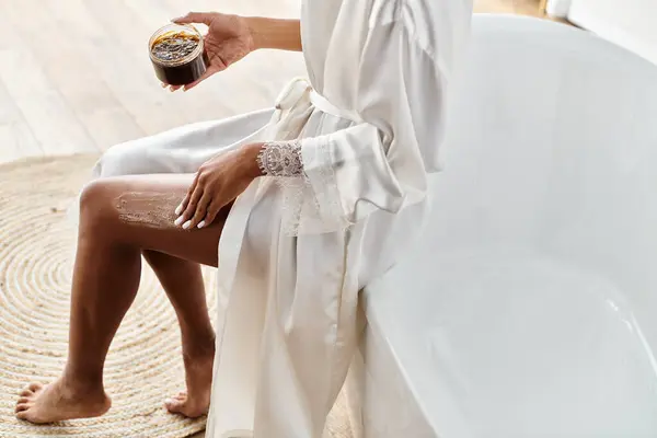 一位非洲裔美国妇女坐在浴缸里 平静地拿着一个罐子 用刷子擦掉了一条腿 — 图库照片