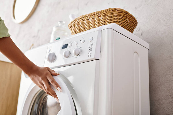 Woman putting a cloth into the dryer in a bathroom while doing laundry.