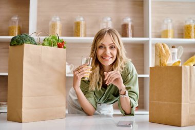 A woman is seated at a table in a kitchen, holding a glass of wine. clipart