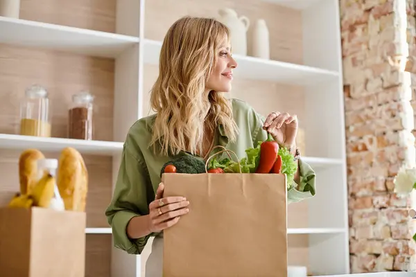 キッチンに立って野菜でいっぱいの食料品袋を持っている女性 — ストック写真