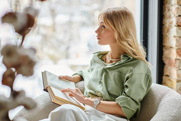 Женщина, сидящая в кресле, читает книгу на кухне.