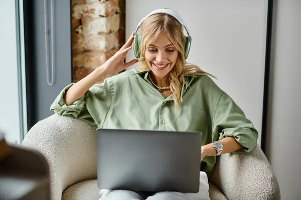 妇女坐在家中的椅子上 使用笔记本电脑 戴着耳机 — 图库照片