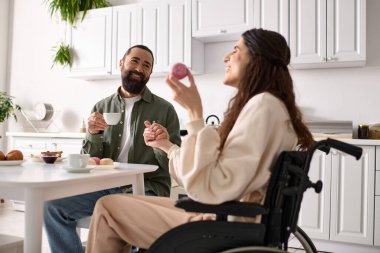 Tekerlekli sandalyeye mahkum neşeli bir kadın yakışıklı kocasıyla kahvaltıda tatlı yiyor.