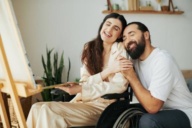 Çekici, hareketli, sakallı, neşeli kocasının yanındaki sehpada resim yapan kadın.
