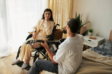 cheerful woman with disability in wheelchair watching her bearded husband playing guitar for her clipart