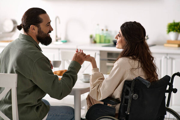 bearded cheerful man enjoying breakfast with his disabled merry wife in wheelchair at breakfast