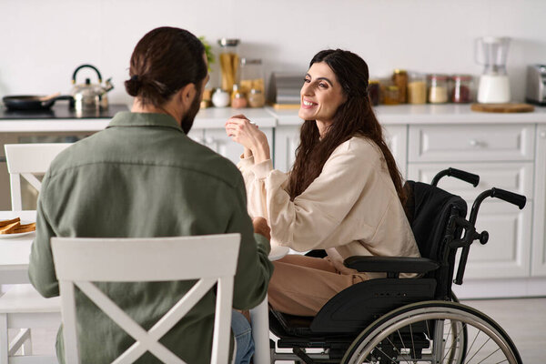 bearded cheerful man enjoying breakfast with his disabled merry wife in wheelchair at breakfast