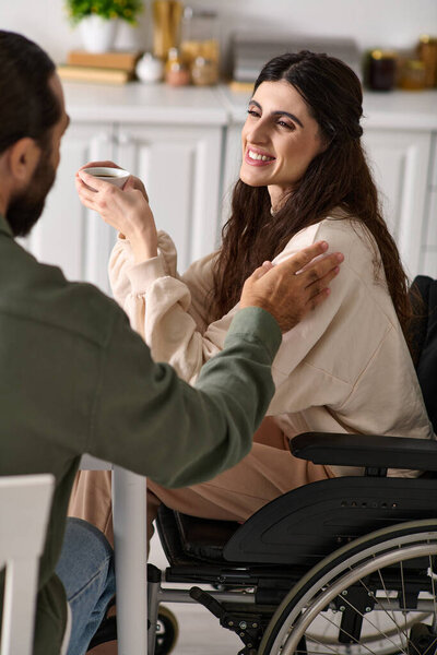 handsome cheerful man enjoying breakfast with his disabled merry wife in wheelchair at breakfast