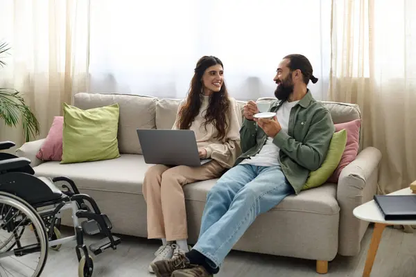 喜怒无常的大胡子男人与残疾漂亮的妻子在笔记本电脑旁共度美好时光 喝咖啡 — 图库照片