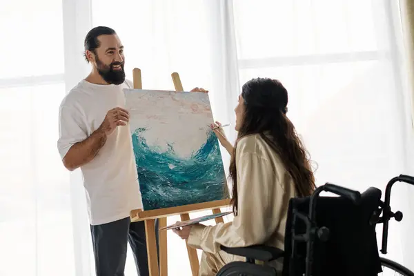 stock image beautiful woman with mobility disability painting on easel next to her cheerful bearded husband