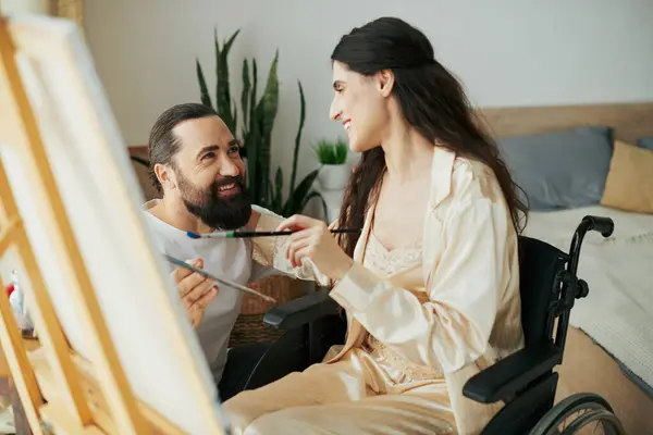 stock image appealing woman with mobility disability painting on easel next to her cheerful bearded husband