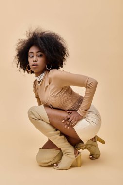 curly african american model in stylish pastel color outfit and thigh-high boots sitting on beige clipart