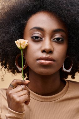 20 'li yaşlardaki şehvetli ve kıvırcık Afrikalı Amerikalı kadın elinde bej arka planda küçük bir gül, şeftali tüyü