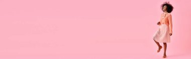 Şeftali rengi bluzlu kıvırcık Afrikalı Amerikalı kadın ve pastel pembe arka planda poz veren midi etek, afiş.