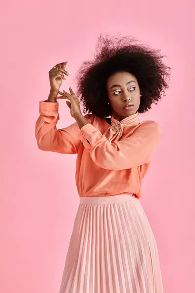 young african american woman in peach blouse, skirt and neck scarf posing on pastel pink background