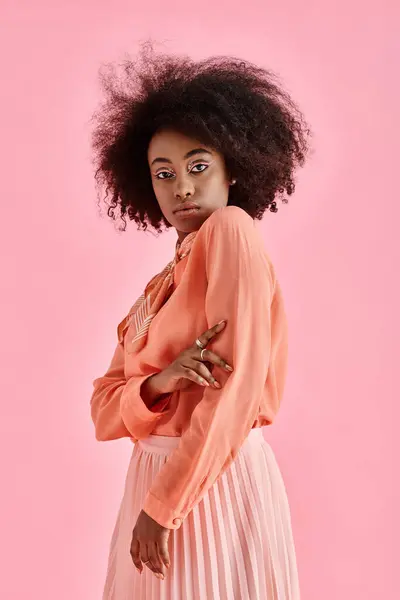 confident african american woman in peach blouse, midi skirt and neck scarf posing on pink backdrop