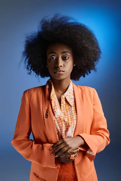 curly african american woman in peach fuzz blazer looking away on gradient blue background