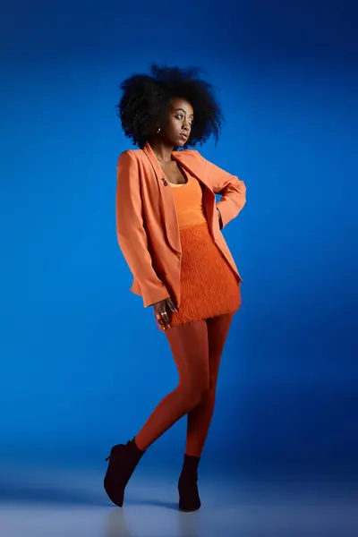pretty african american model in textured dress and blazer posing with hand on hip on blue