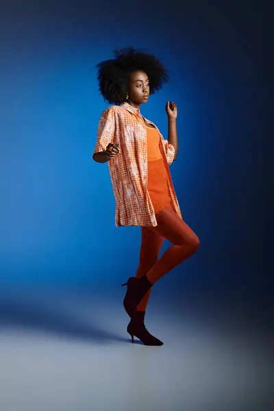 stock image Chic look of pretty african american model in patterned shirt and orange dress on blue background