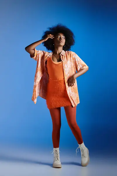 fashionable african american model in patterned shirt and textured dress posing on blue backdrop