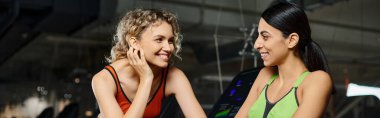 Çekici bayan koç ve spor giyim müşterisi spor salonunda koşu bandında egzersiz yapıyorlar.