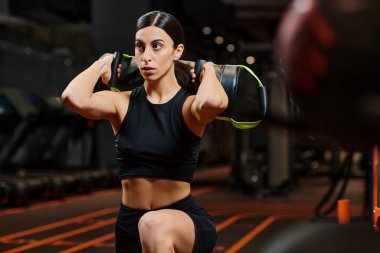 Spor elbiseli esmer, çekici bir kadın spor salonunda spor çantasıyla aktif egzersiz yapıyor.