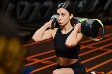 Spor elbiseli, esmer, çekici atletik kadın spor salonunda spor çantasıyla aktif egzersiz yapıyor.