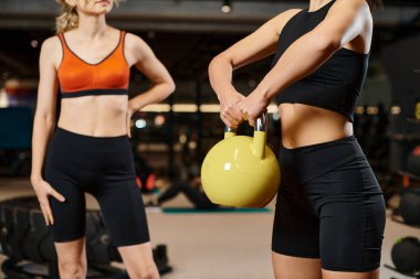 Spor salonunda bayan koçunun yanında kettlebell egzersizi yapan atletik kadın manzarası.