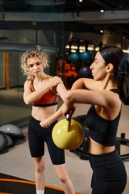 Spor giyim bölümündeki enerjik çekici koç müşterisini spor salonunda kettlebell kullanırken izliyor.