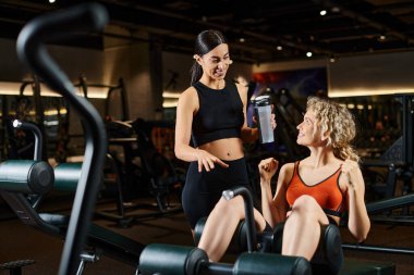 Neşeli atletik bayan antrenör sarışın güzel bir kadına danışmanlık yapıyor spor salonundayken nasıl sıkacağını öğretiyor.