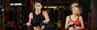 Sporcu enerjik bir kadın spor salonunda spor salonunda atletik bayan koçunun yanında modern çapraz antrenör kullanıyor.