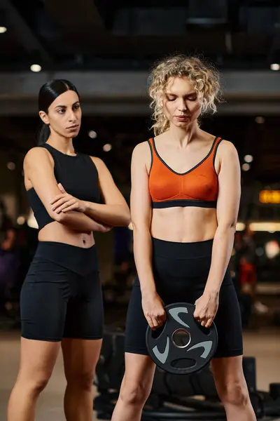 stock image appealing athletic female coach in black sportwear explaining how to use weight plate to her client