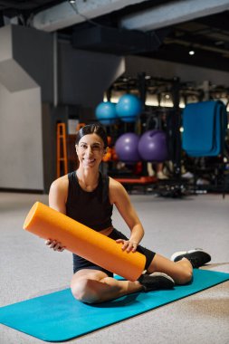 Keyifli çekici atletik kadın spor salonunda spor paspası üzerinde geriniyor ve kameraya gülümsüyor.