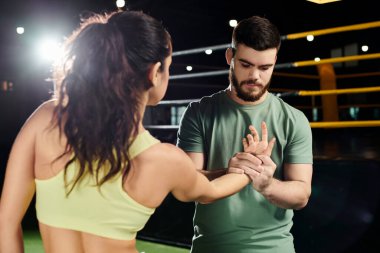 Erkek bir antrenör, spor salonunda yan yana duran bir kadına savunma teknikleri öğretiyor..
