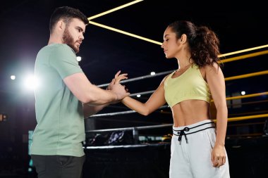 Bir erkek eğitmen, bir kadına spor salonunda savunma teknikleri öğretiyor..